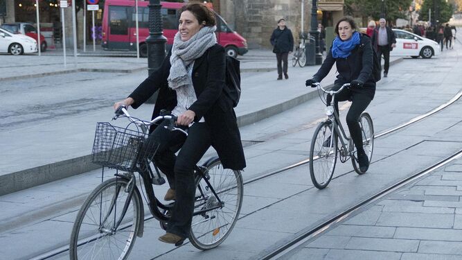 Dos ciclistas abrigadas con bufandas cruzan la Avenida de la Constitución.