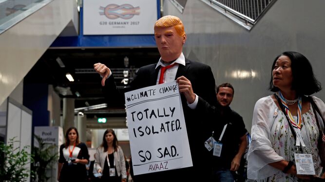 Un asistente a la cumbre del G-20 en Hamburgo disfrazado de Donald Trump sostiene un cartel de protesta contra el cambio climático.