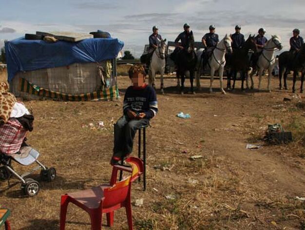 Un ni&ntilde;o, en un taburete en el asentamiento con seis agentes a caballo detr&aacute;s.

Foto: Jose Angel Garcia - Victoria Hidalgo