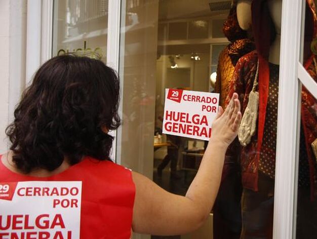 Una mujer coloca un cartel de la huelga en el escaparate de un comercio.

Foto: Bel&eacute;n Vargas
