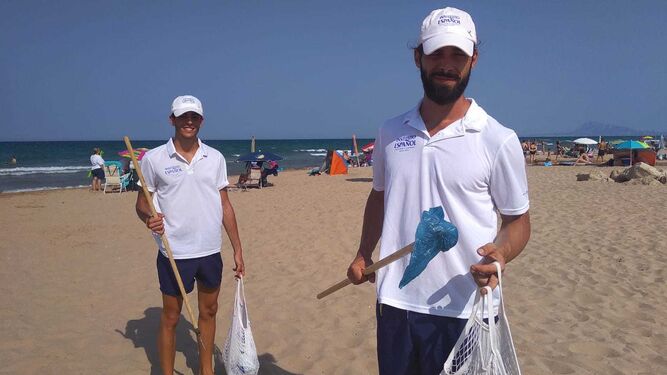 Dos voluntarios reparten bolsas en la playa.