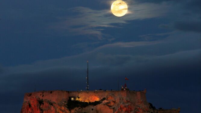 La luna llena asoma entre las nubes, por encima del Castillo de Santa B&aacute;rbara de Alicante.