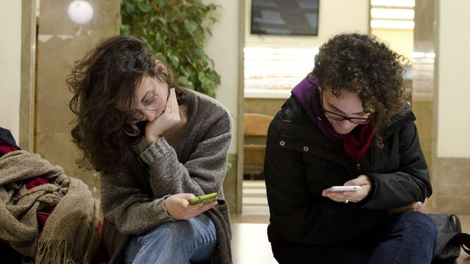Dos jóvenes, pendientes de sus móviles