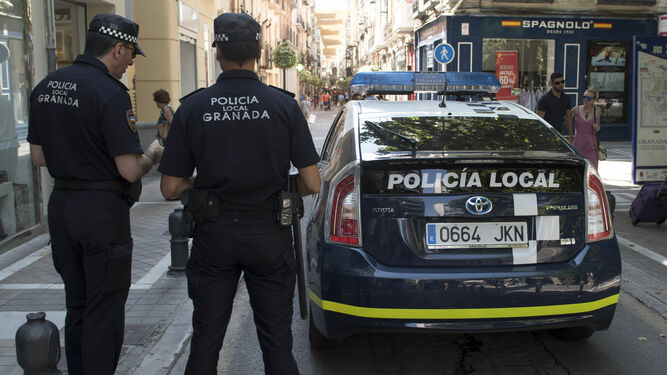 Imagen de archivo de dos agentes de la Policía Local de Granada junto a un coche patrulla.