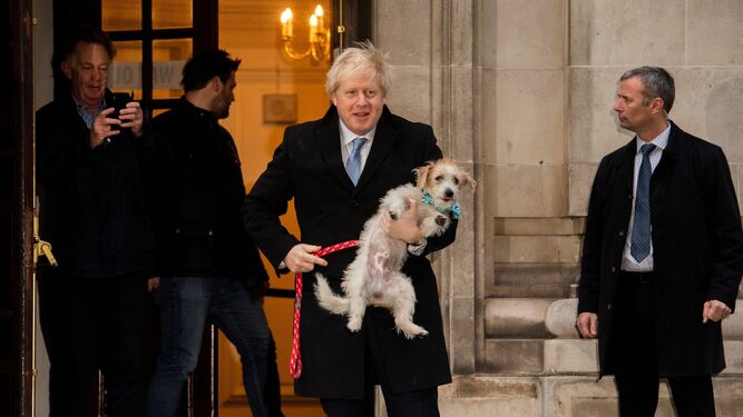 Boris Johnson sale de un centro de votación con su perro en brazos.