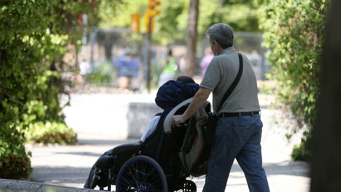 Una persona pasea a un joven en silla de ruedas