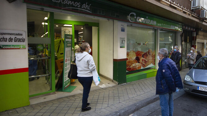 Clientes aguardan en la cola para entrar a comprar en el supermercado Covirán de Ancha de Gracia de Granada.