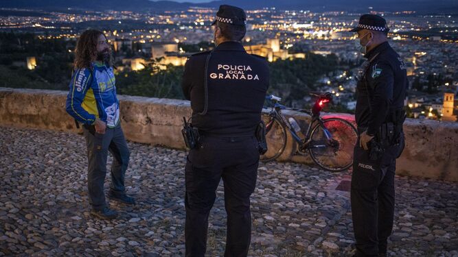 Dos agentes de la Policía Local de Granada conversan con un ciclista en la ciudad.