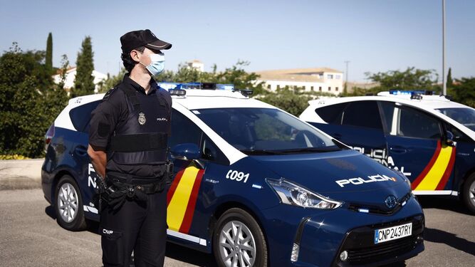 Un agente de la Policía Nacional de Granada junto a vehículos policiales.