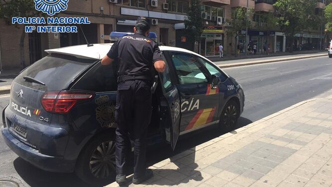 Un agente de la Policía Nacional junto a un coche policial en la zona Norte de Granada.
