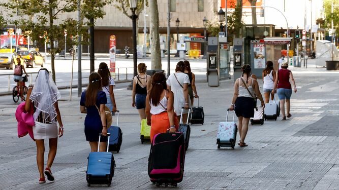 Turistas caminando por la Plaza Cataluña de Barcelona con sus maletas.