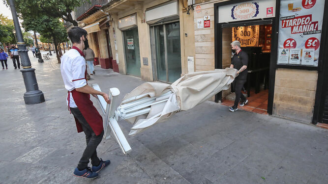 Dos trabajadores recogen la terraza de un bar en el centro de Jerez.