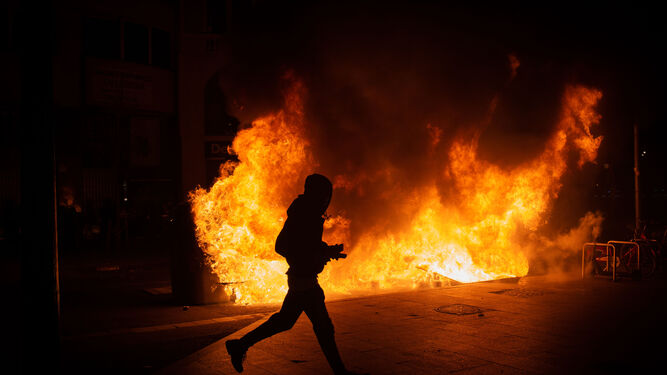 Un manifestante pasa corriendo delante de una barricada en llamas