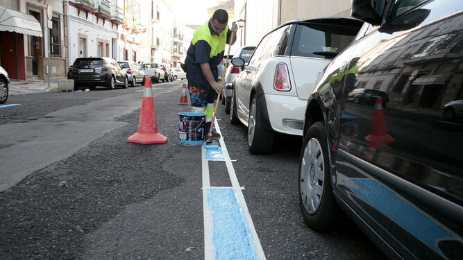 Imagen de archivo de un operario pintando una línea azul de aparcamiento.