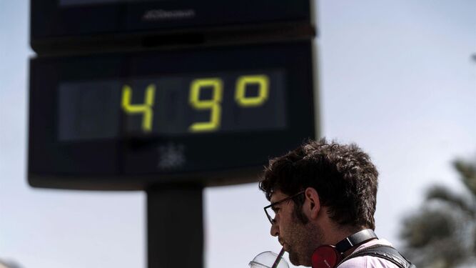 Un hombre bebiendo junto a un termómetro en medio de una ola de calor
