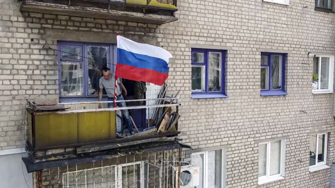 Un hombre coloca una bandera rusa en su balcón en Lisichansk.