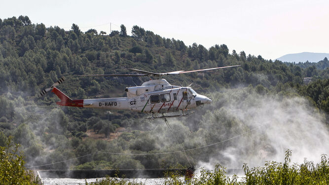 Un helicóptero carga agua para dirigirse al frente del incendio en Les Useres, Castellón