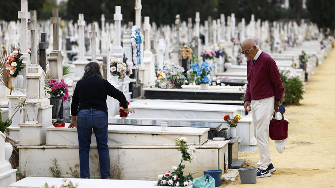 Dos personas adecentan una tumba de suelo en el cementerio de Sevilla.