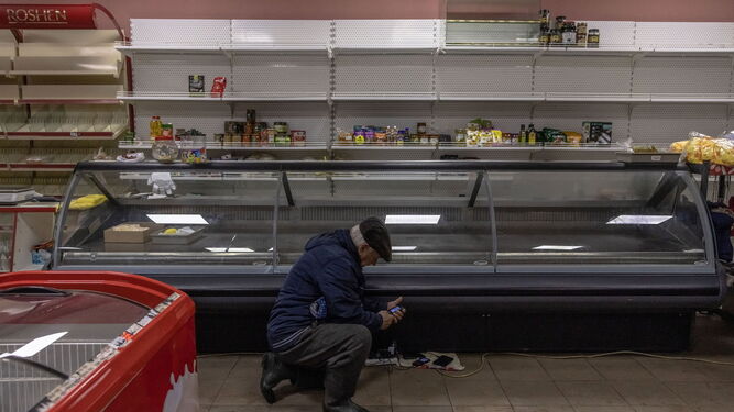 Un ucraniano trata de cargar su móvil ante un estante prácticamente vacío de un supermercado de Jerson.