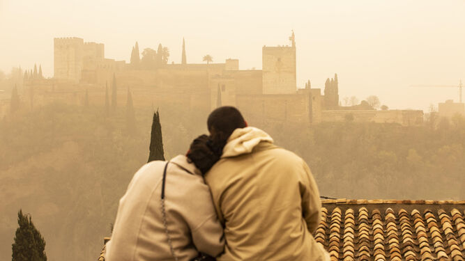 Una pareja en un mirador ante una Alhambra teñida por la calima.