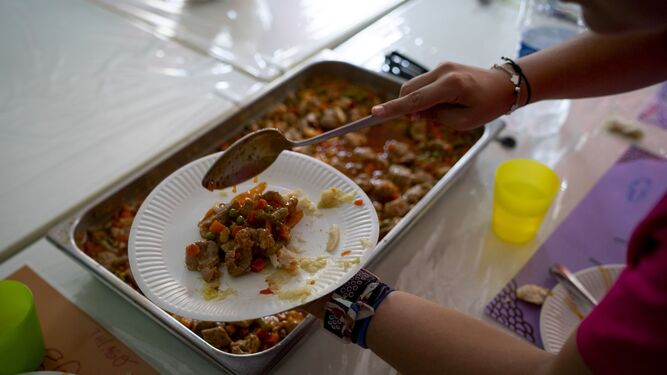 Una monitora de comedor sirve un plato a un escolar