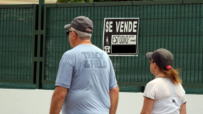 Dos personas pasan frente a un cartel de 'Se Vende' en Granada