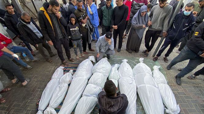 Un grupo de personas rodea los cuerpos tapados de varias víctimas en Rafah.