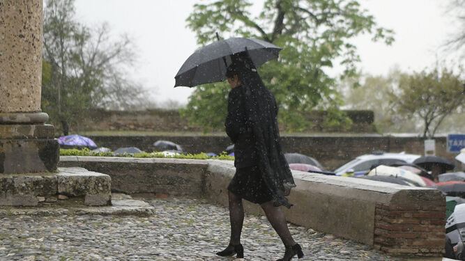 Una camarera camina rápido hacia la iglesia de su hermandad cubierta por un paraguas