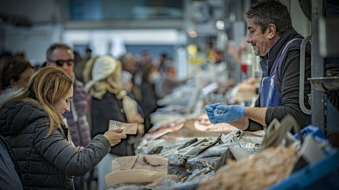 Una mujer paga en efectivo al tendero de una pescadería en un mercado